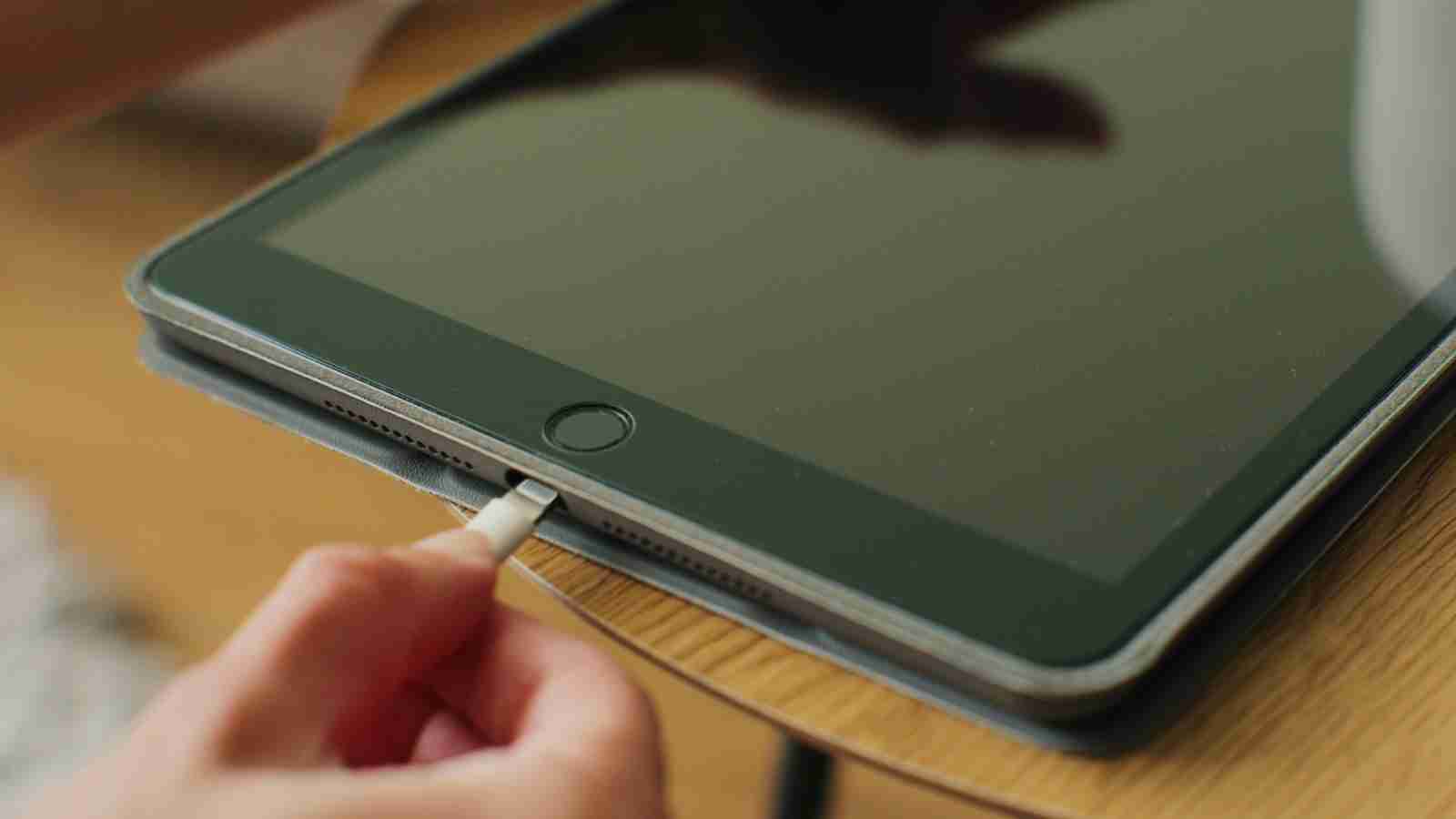 A hand plugs a charging cable into a tablet computer.