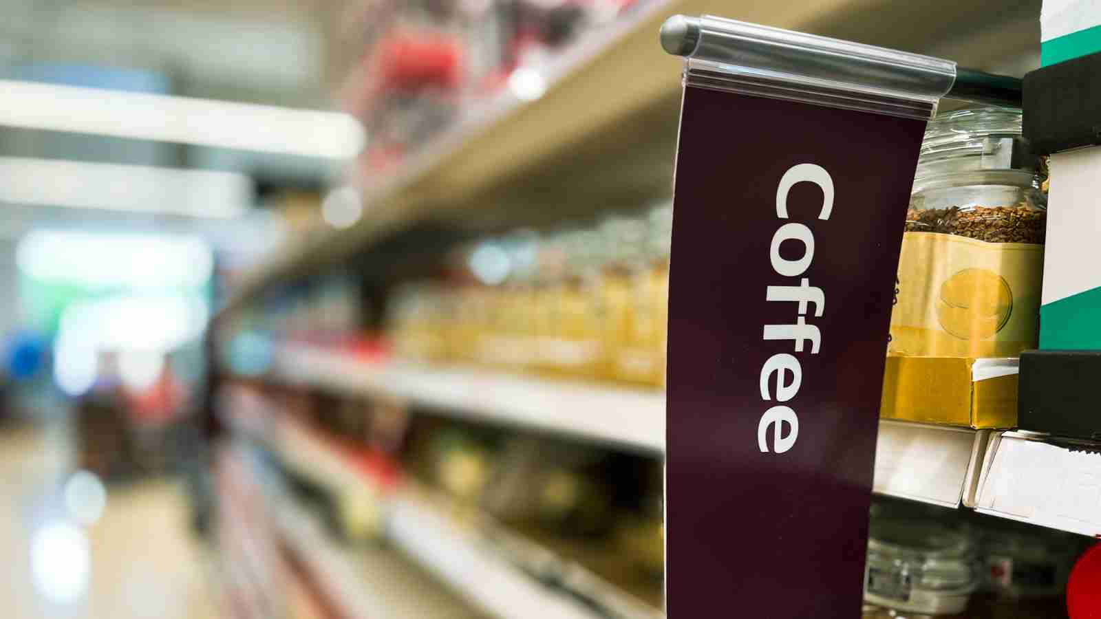 A "Coffee" sign hangs from a supermarket shelf displaying various coffee products.