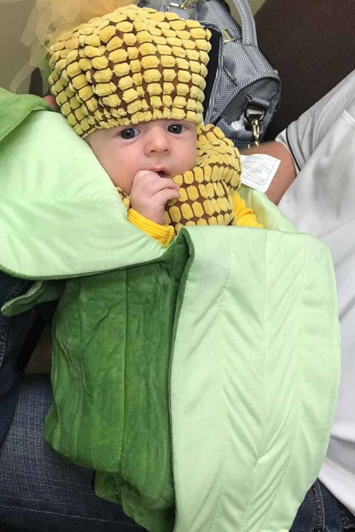 Baby dressed in a yellow and green cloth imitating a corn fruit.