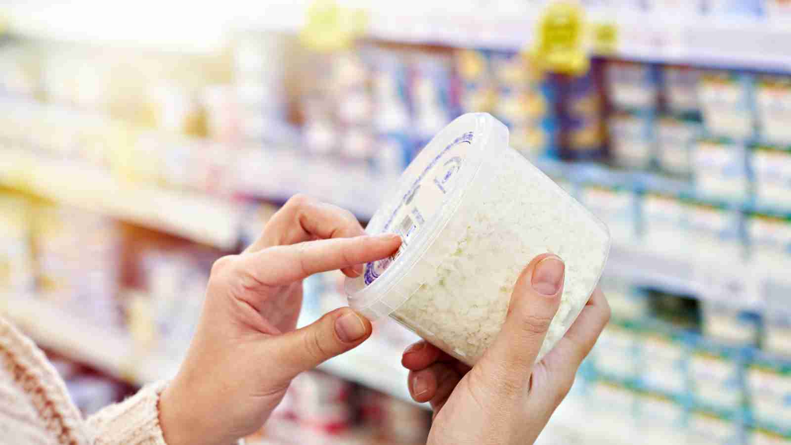 A person examines a container of cottage cheese in a supermarket aisle.