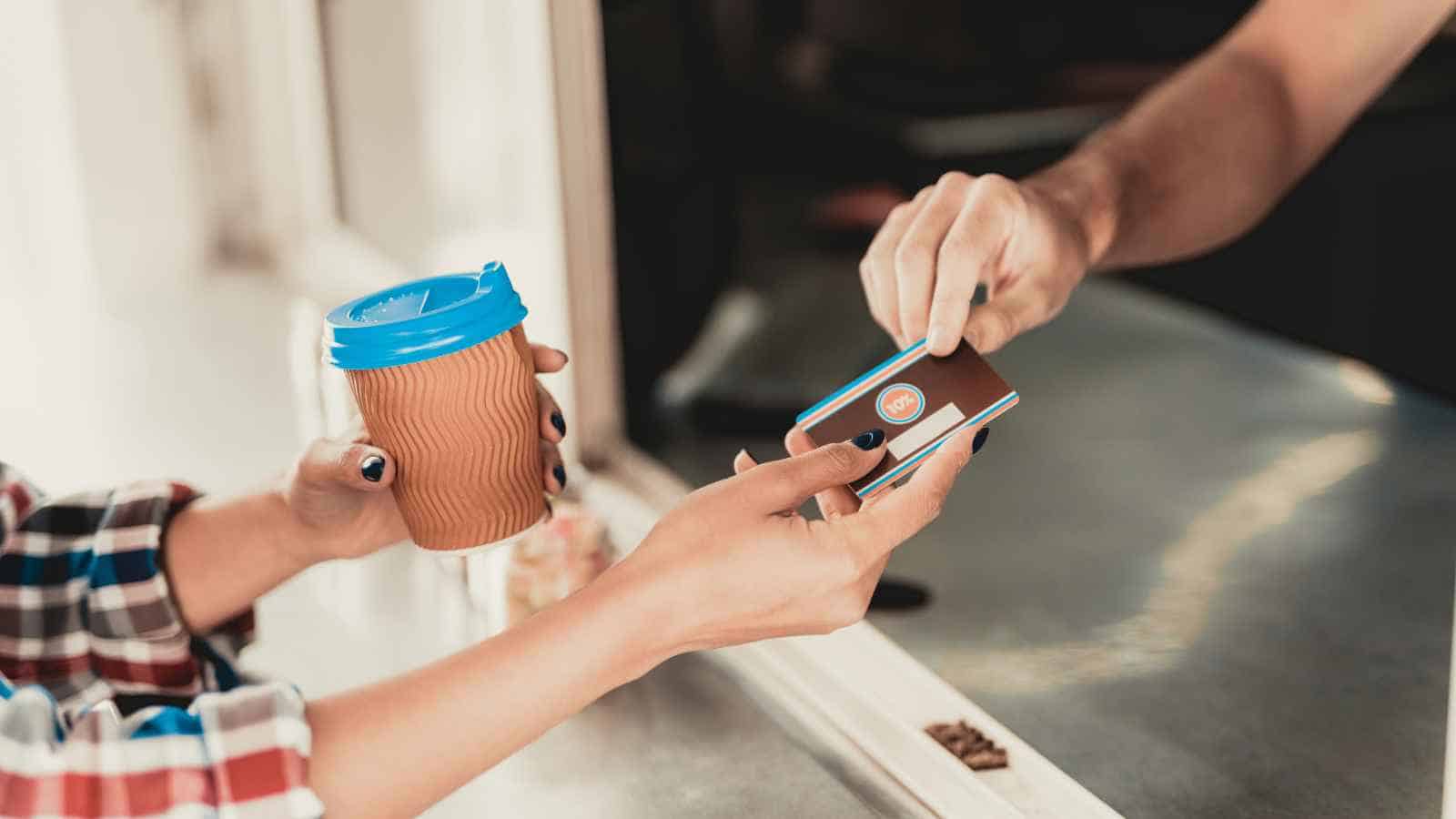 A customer hands a credit card to a vendor at a food truck window while receiving a coffee.