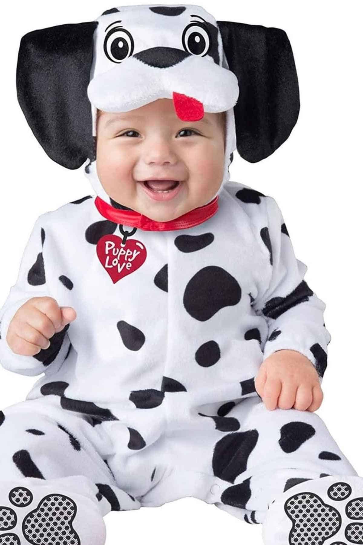 A baby dressed in a Dalmatian puppy costume with black spots, floppy ears, a red collar, and a "Puppy Love" tag, smiling at the camera.