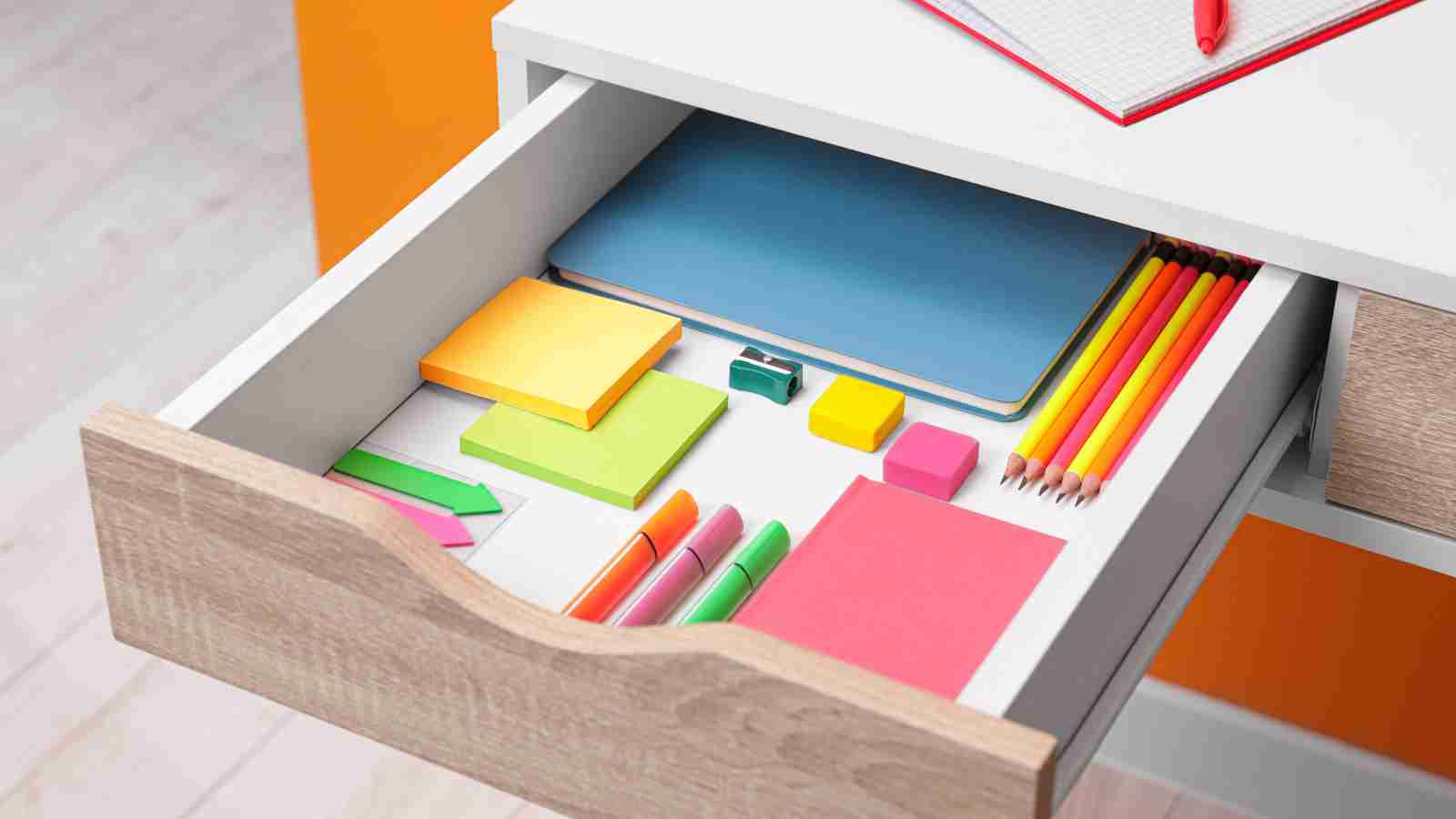 A desk drawer is open, revealing a neatly organized collection of stationery items, including colored pencils, sticky notes, and markers.