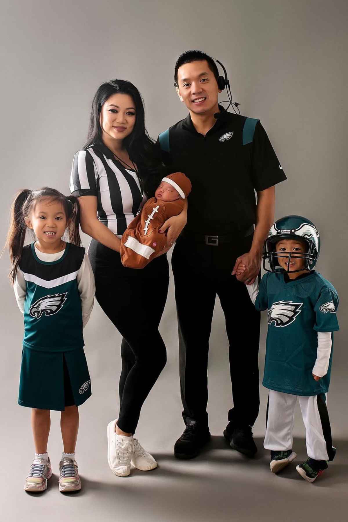 A family in a costume, Dad wearing as a coach, Mom as a referee, daughter as a cheerleader, son as a football player and a little one wears as a football.