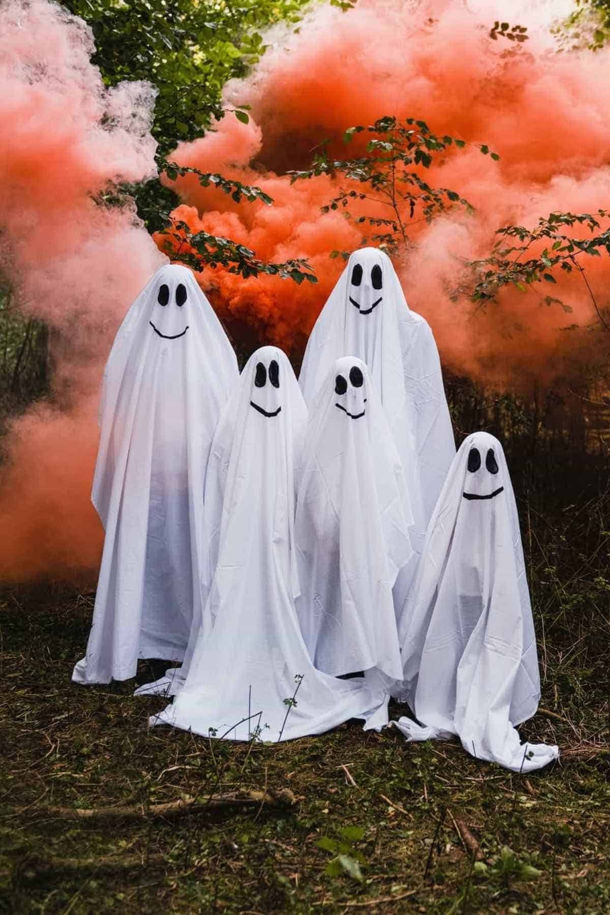 A family of five in simple yet creepy all-white ghost costumes, standing together with an eerie orange smoke behind them.