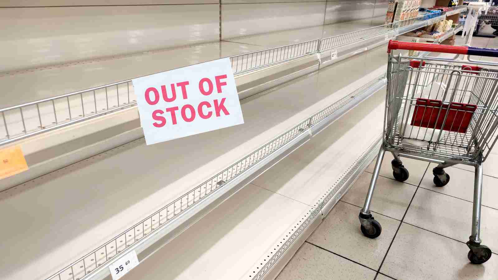 An empty supermarket shelf with an "OUT OF STOCK" sign is next to an empty shopping cart.