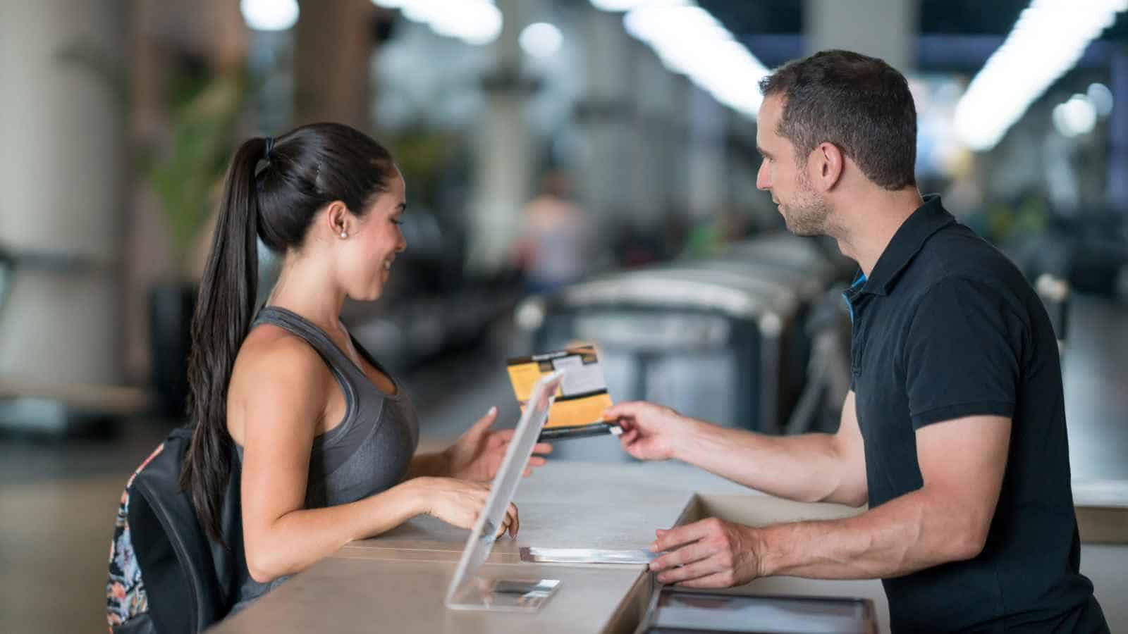 A woman smiles as a man at a counter hands her a document.