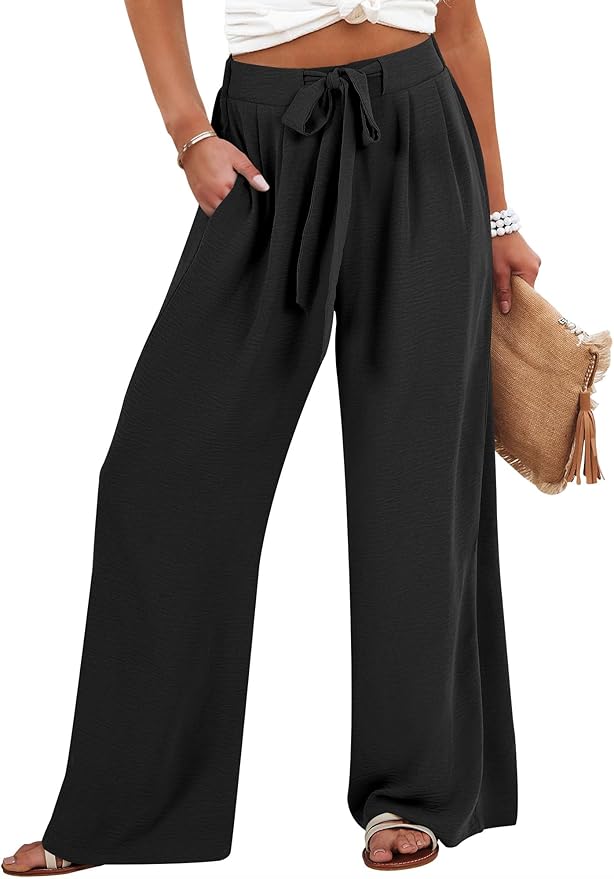 Woman wearing high-waisted, wide-leg black pants with a tie belt, white top, sandals, beaded bracelet, and holding a fringed clutch bag.