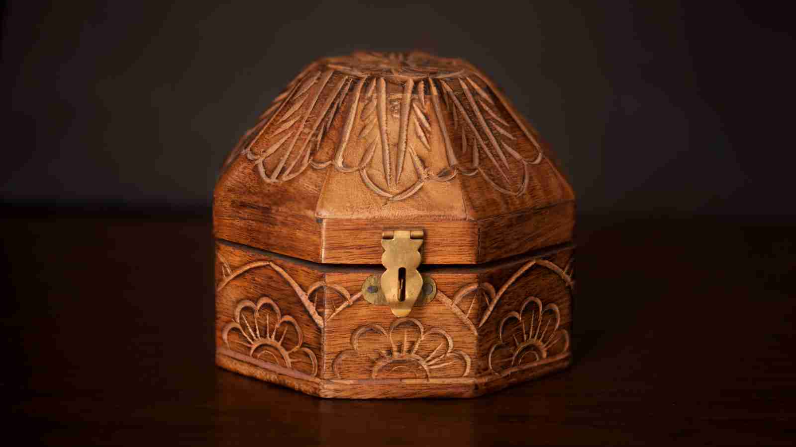 A small, intricately carved wooden box with a brass clasp sits on a dark wooden surface.