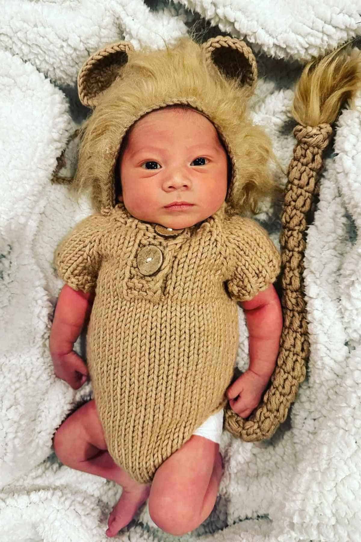A baby lying in bed wearing a knitted lion costume.
