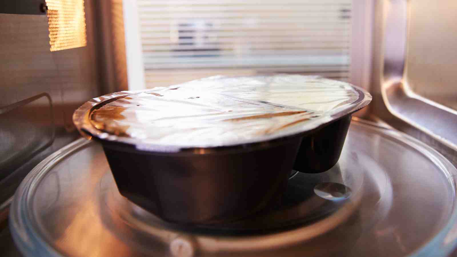 A plastic food container with a plastic film cover is inside a microwave oven.
