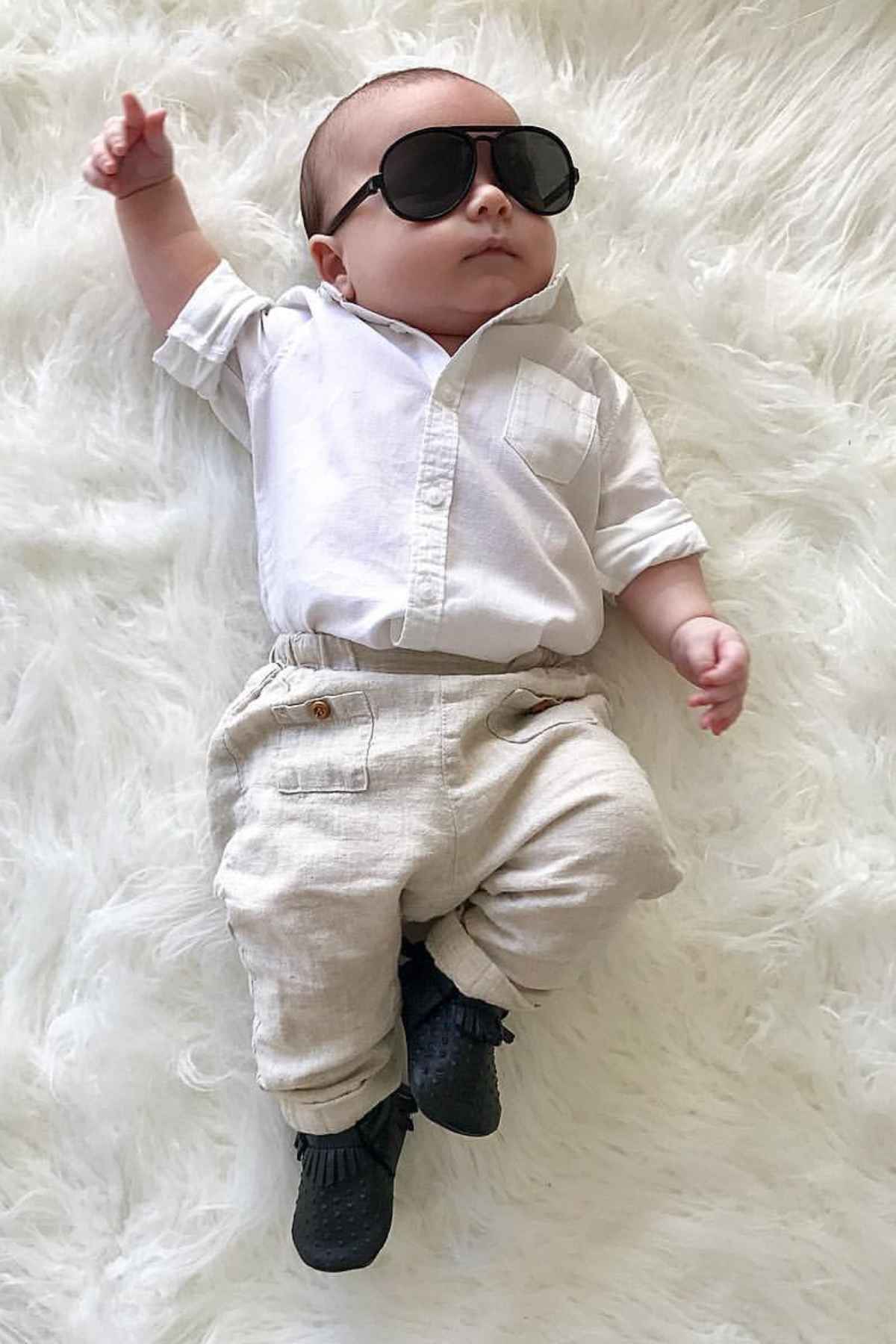 A baby wearing sunglasses, white collar long sleeve and white pants, dressed as Mr. Worldwide.