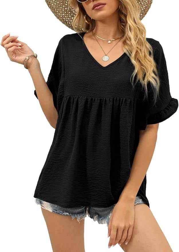 Woman wearing a black short-sleeve V-neck blouse, denim shorts, a sun hat, sunglasses, and jewelry, posing with one hand raised.