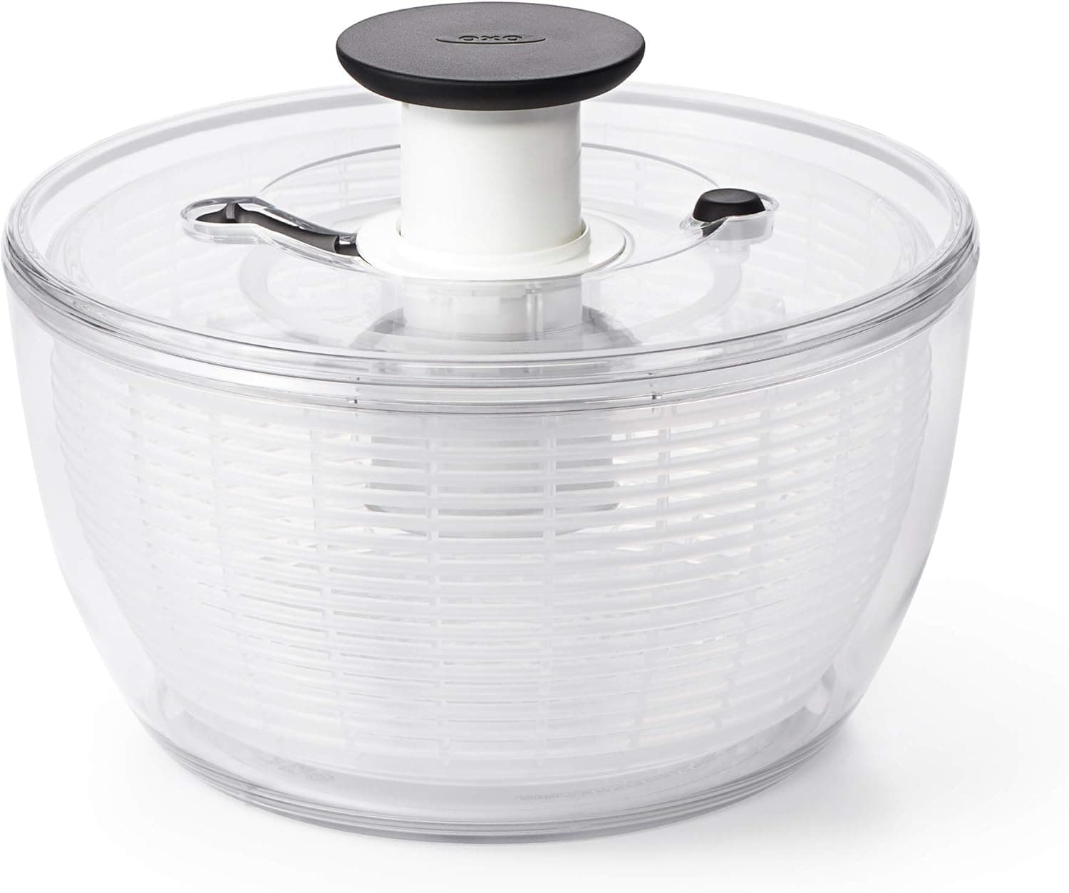 A clear plastic salad spinner with a central spinning mechanism and a black push button on top.