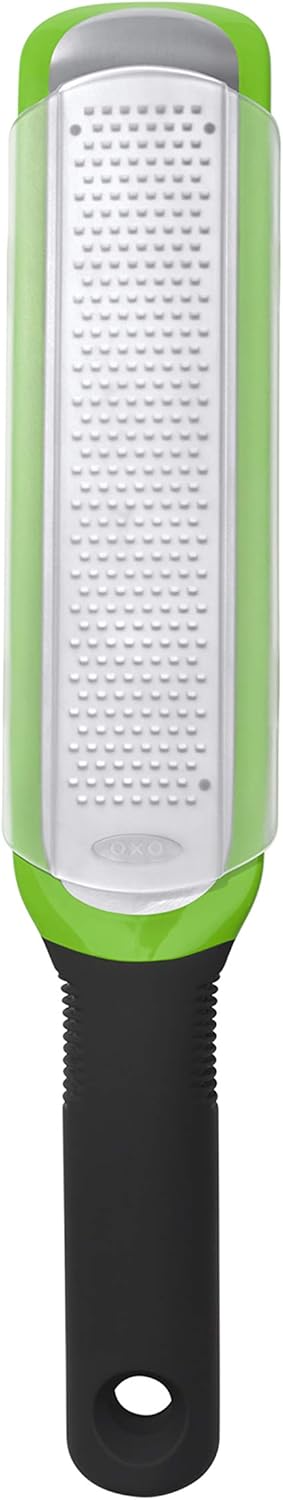 A handheld kitchen grater with a green frame, silver grating surface, and a black handle featuring a hole for hanging.
