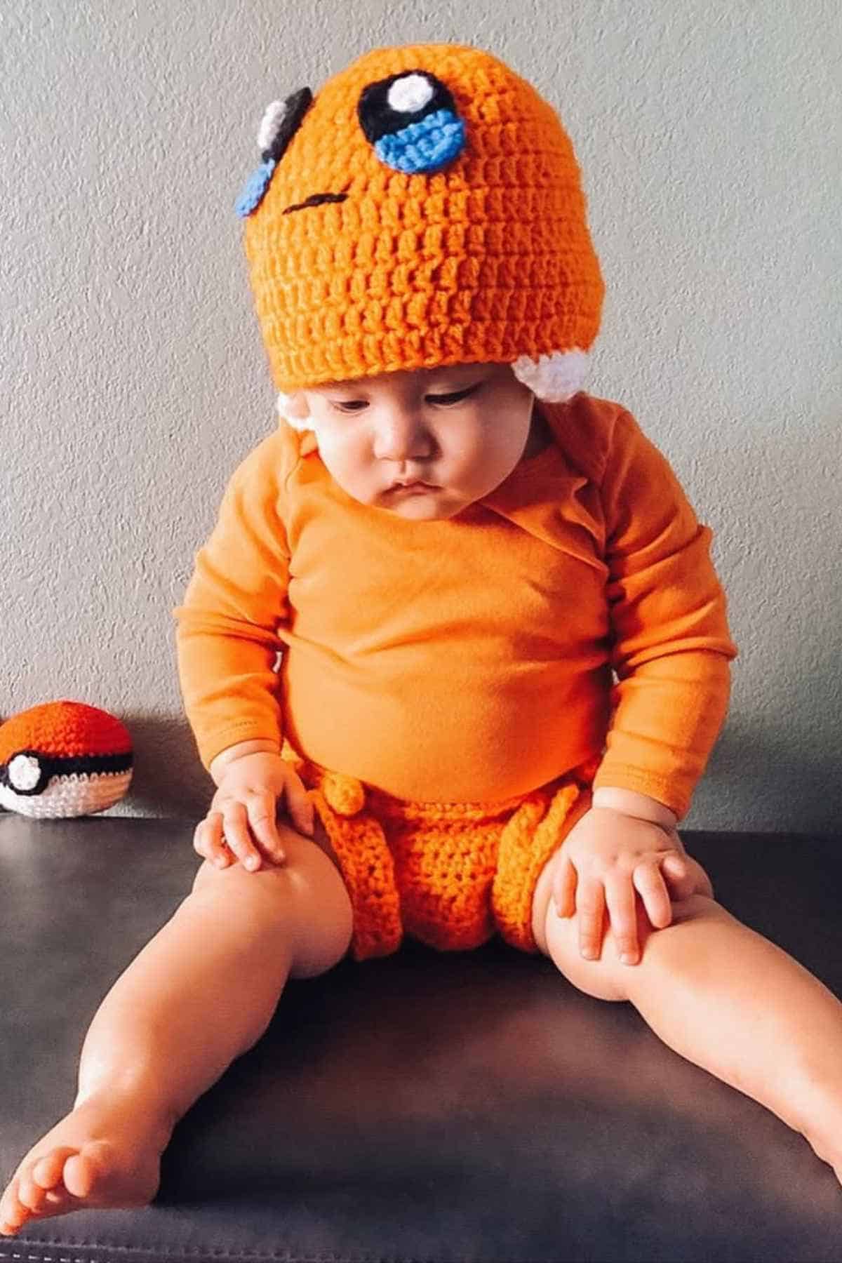 Baby sitting on a wooden surface dressed as a pokemon, surround him is one pokemon ball.
