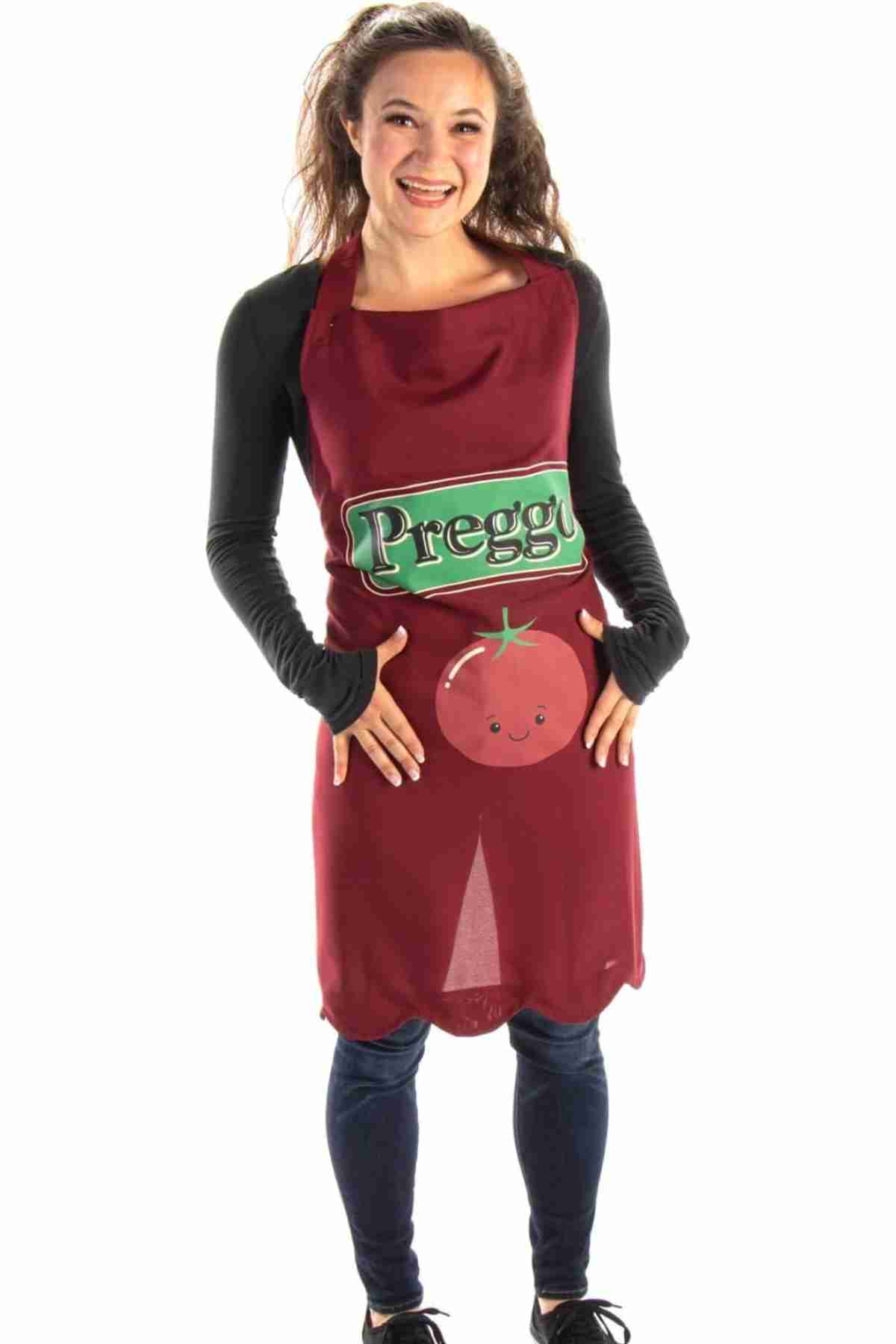 Woman wearing a maroon apron with "Preggo" text and a cartoon tomato, smiling and standing against a white background.