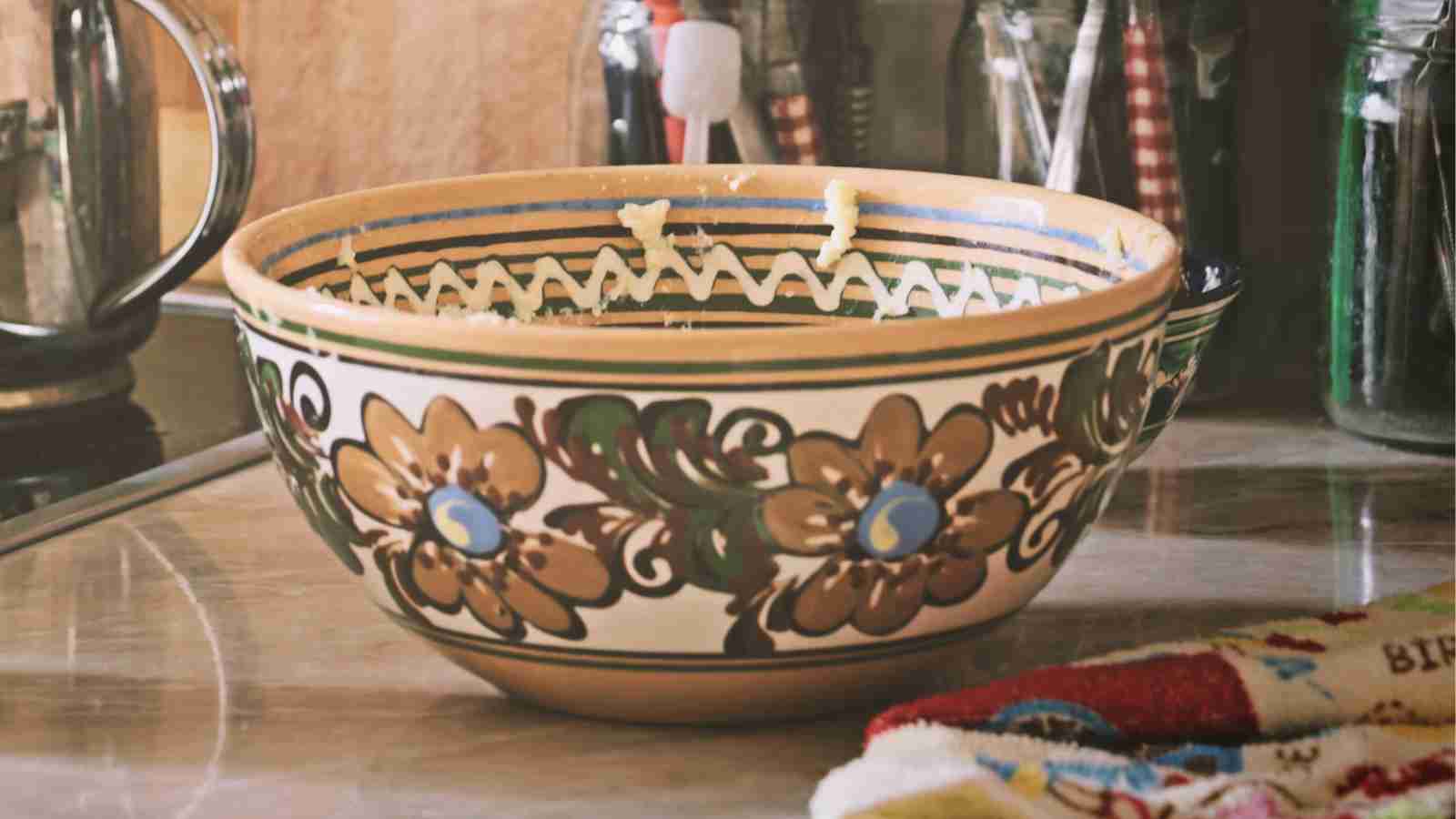 A large, decorated ceramic bowl sits on a countertop next to a tea kettle and some jars.