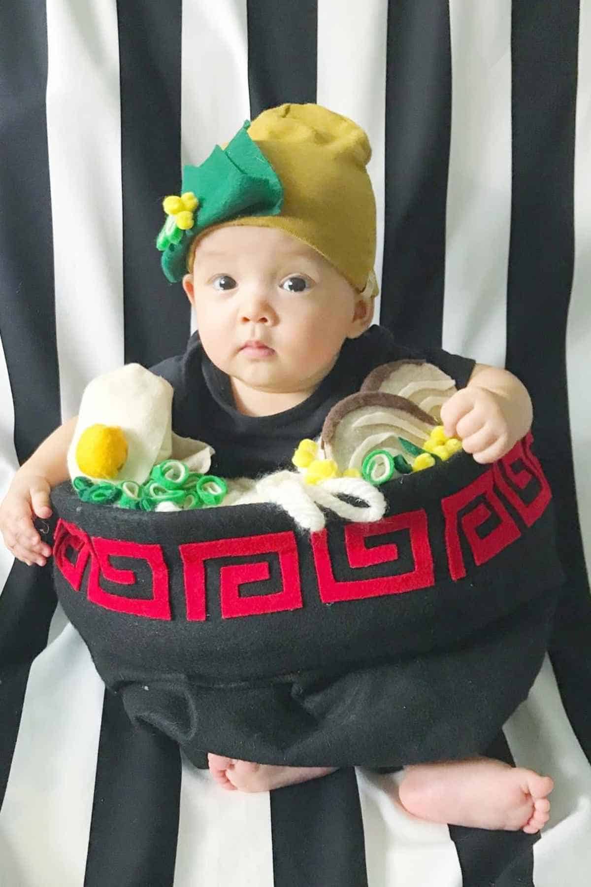 A baby seated in a bowl of ramen behind him is a black and white vertical stripe background.