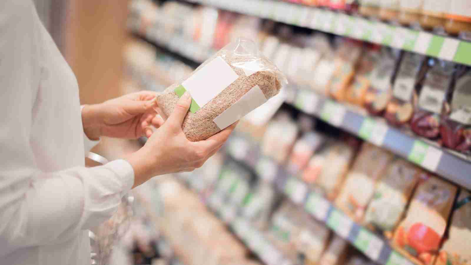 A person in a white shirt reads the label on a bag of grains in a grocery store.