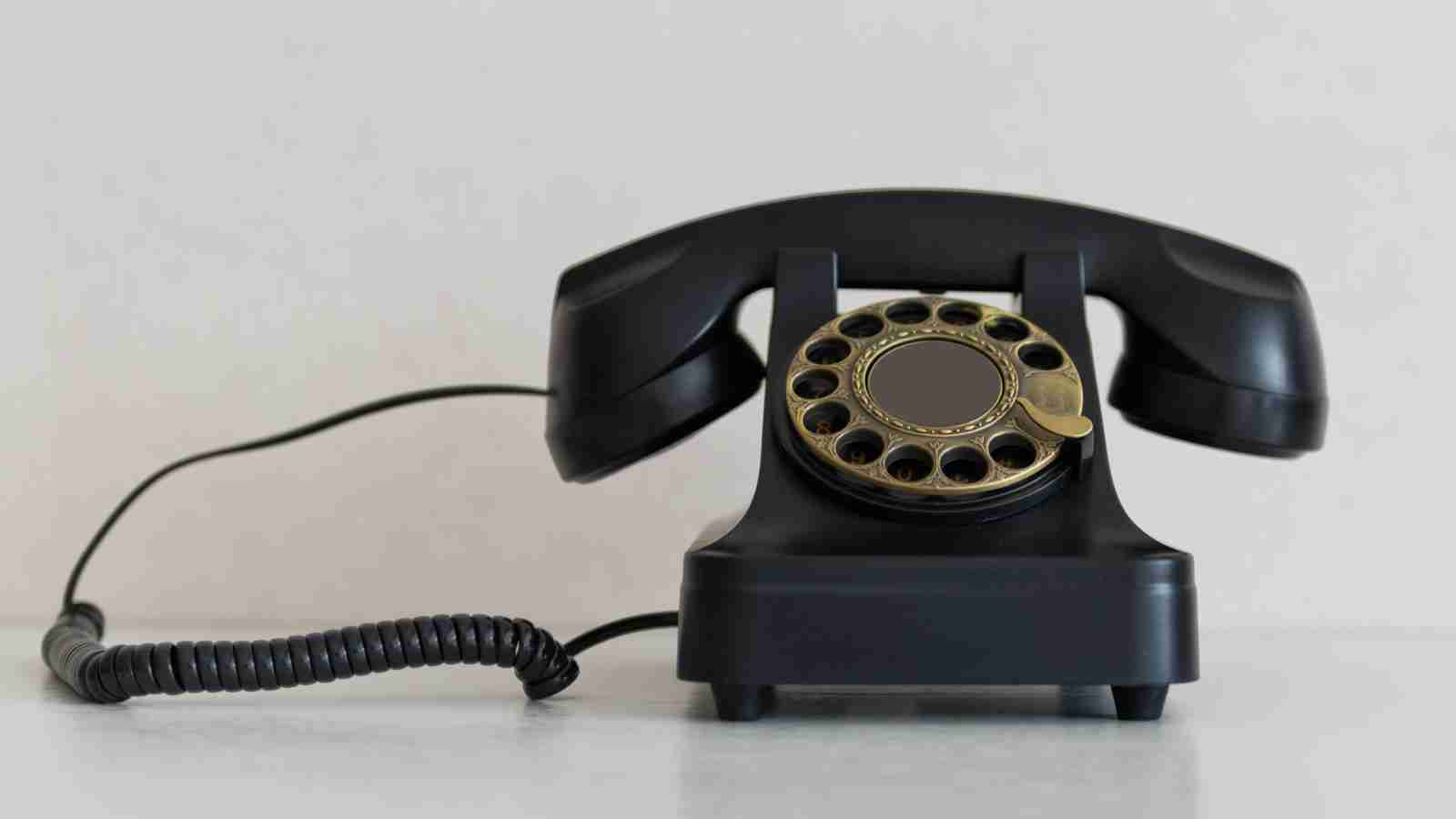 A vintage black rotary telephone with a brass dial sits on a white surface.