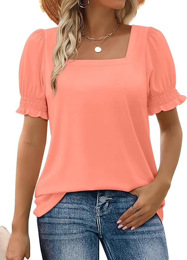 Woman wearing a peach-colored, short-sleeve, square-neck blouse with ruffled sleeves and blue jeans, standing with one hand in her pocket.