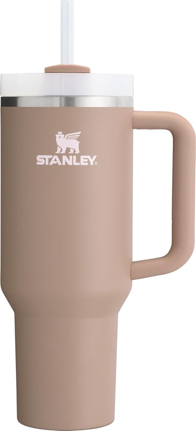 A tan Stanley stainless steel travel tumbler with a handle, clear lid, and straw, shown against a plain white background.
