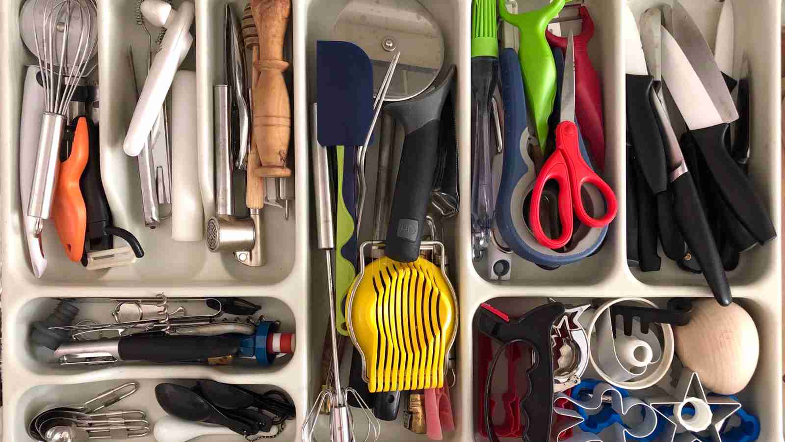 A kitchen utensil drawer is overflowing with various cooking tools and gadgets.
