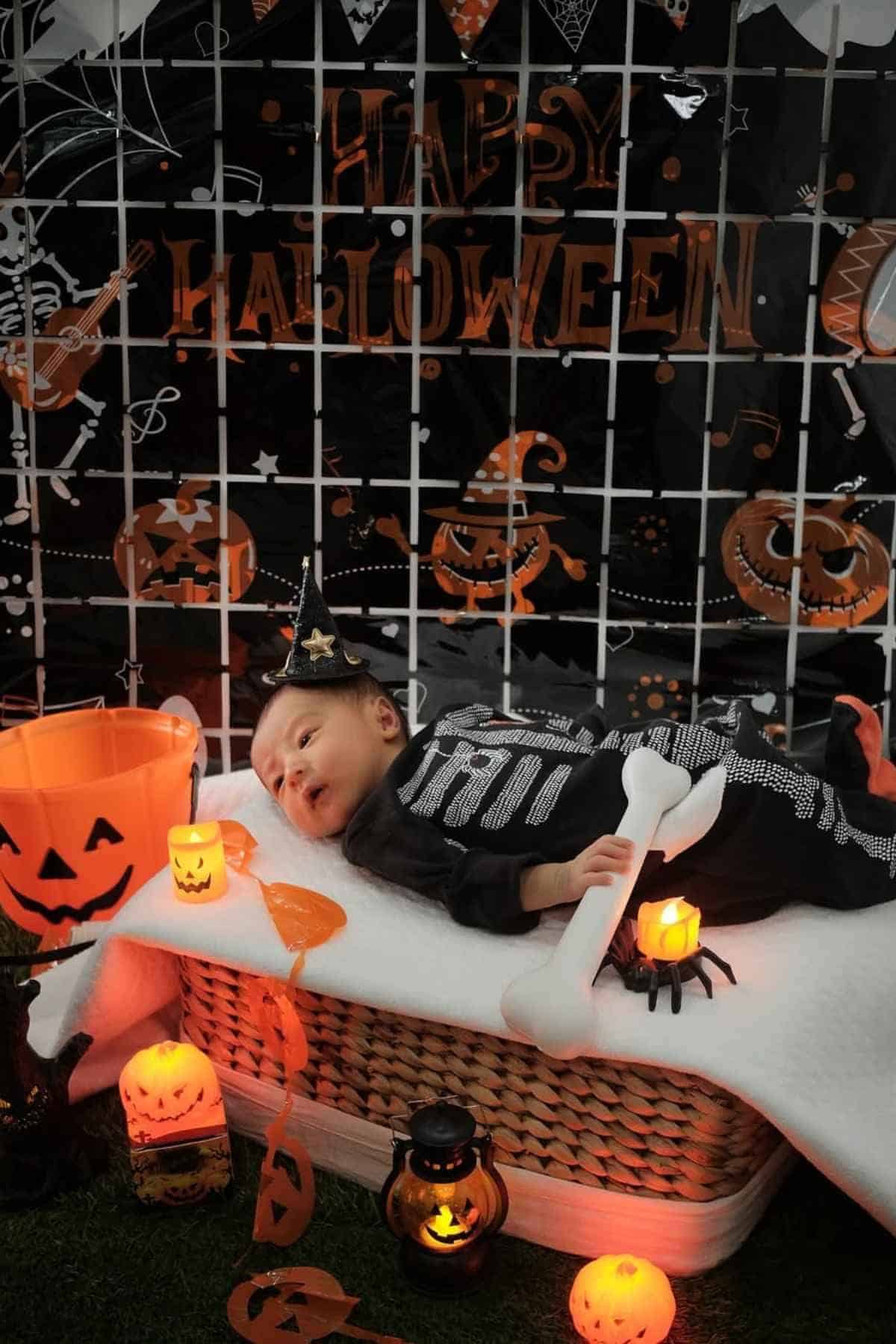 Baby dressed in a classic skeleton costume lying on bed while holding a bone-shaped toy.