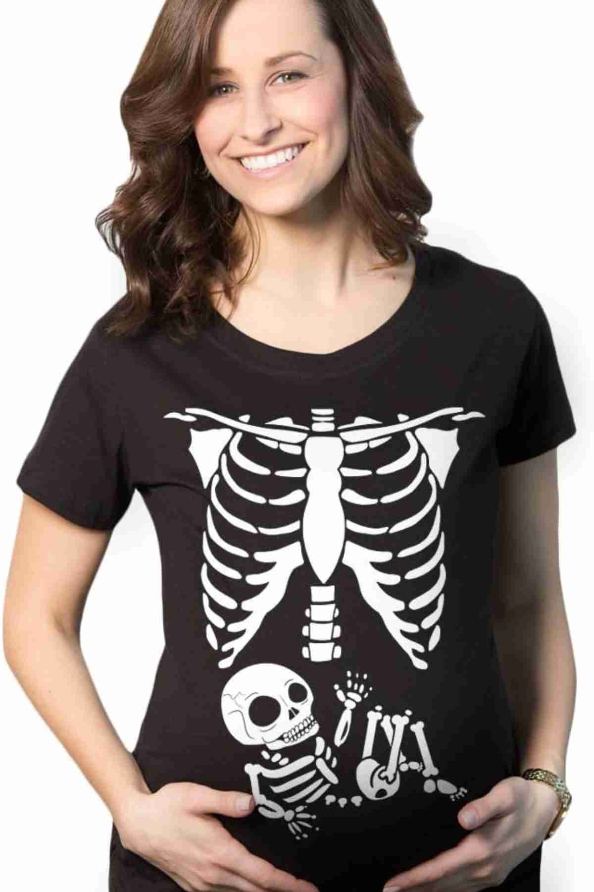 A smiling woman wears a black shirt with a white skeleton print, including a small baby skeleton graphic over her stomach.
