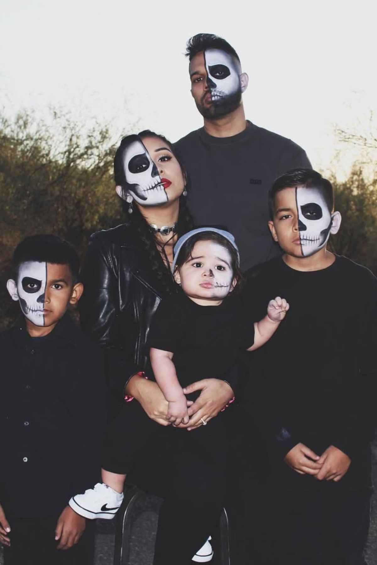 A family of five wearing all black and painted their half faces with skull.