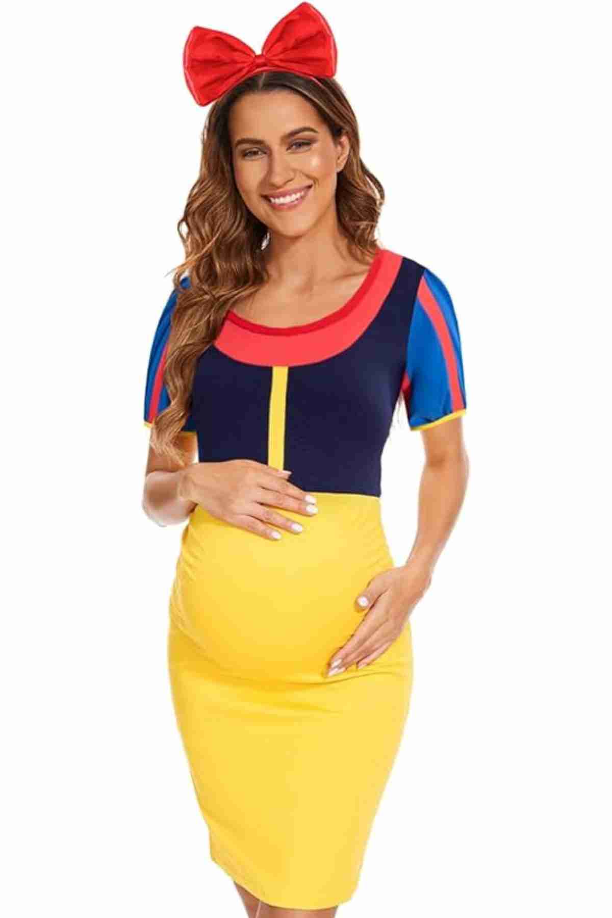 A pregnant woman wearing a Snow White-inspired dress and a large red bow headband, smiling with one hand on her bump.