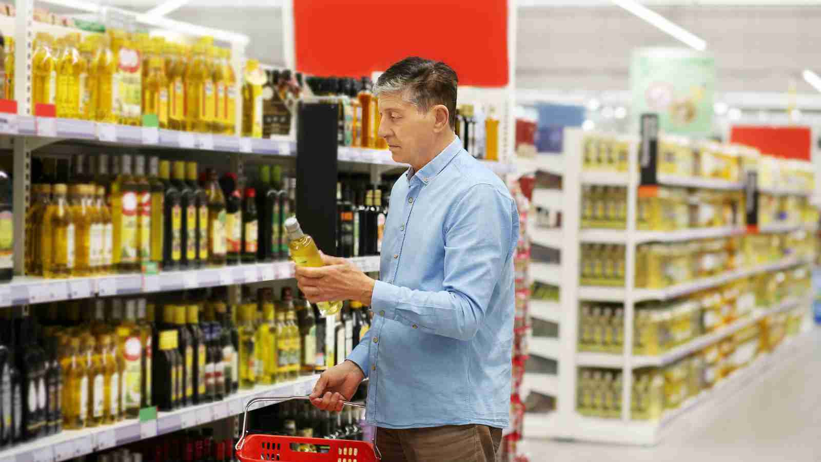 A man in a blue shirt examines a bottle of vinegar on a supermarket shelf.