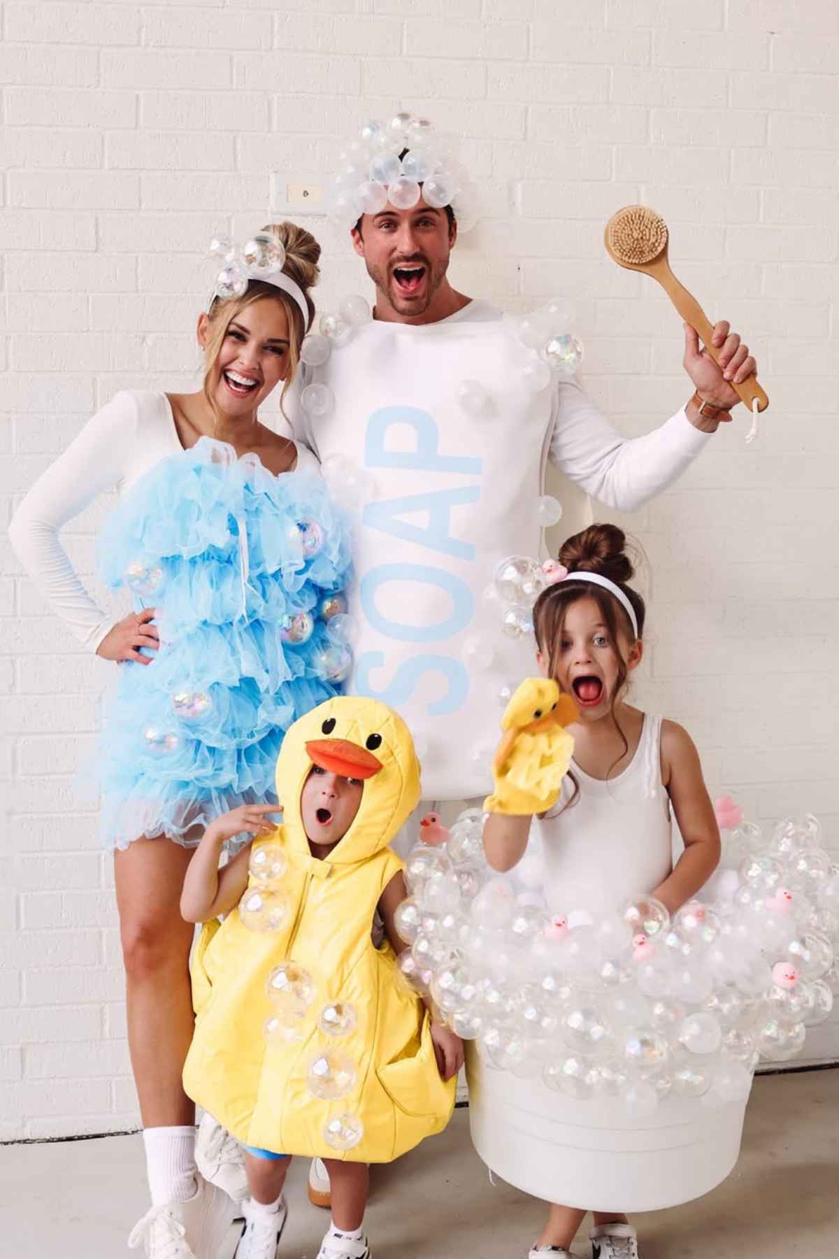 A family in costume: a woman in a blue loofah outfit, a man in a white "soap" costume, a child in a duck costume, and a child dressed as a bubble bath with plastic bubbles.