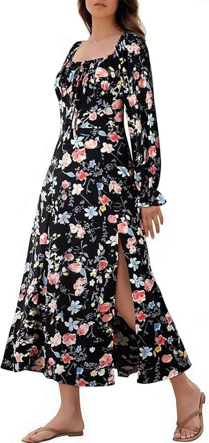 A woman wearing a long-sleeve, black floral dress with a side slit and flat sandals, standing against a white background.