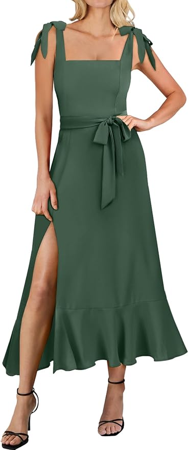 Woman wearing a sleeveless, dark green maxi dress with a square neckline, tie shoulder straps, waist belt, thigh-high slit, and ruffled hem, paired with black heeled sandals.