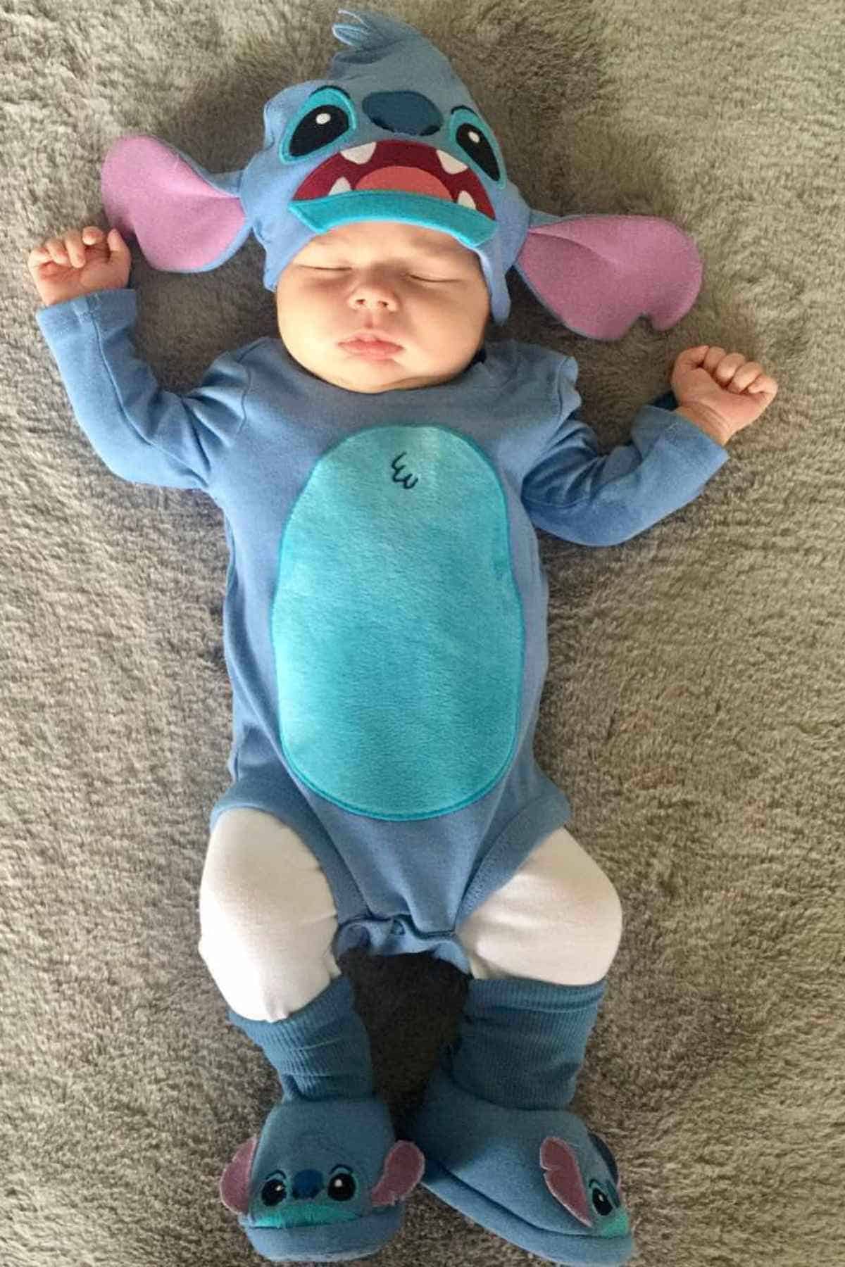 A baby on bed, dressed as Stitch with closed eyes.