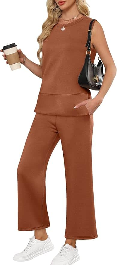 A woman wearing a sleeveless brown top and matching wide-leg pants, holding a coffee cup, carrying a black shoulder bag, and wearing white sneakers.