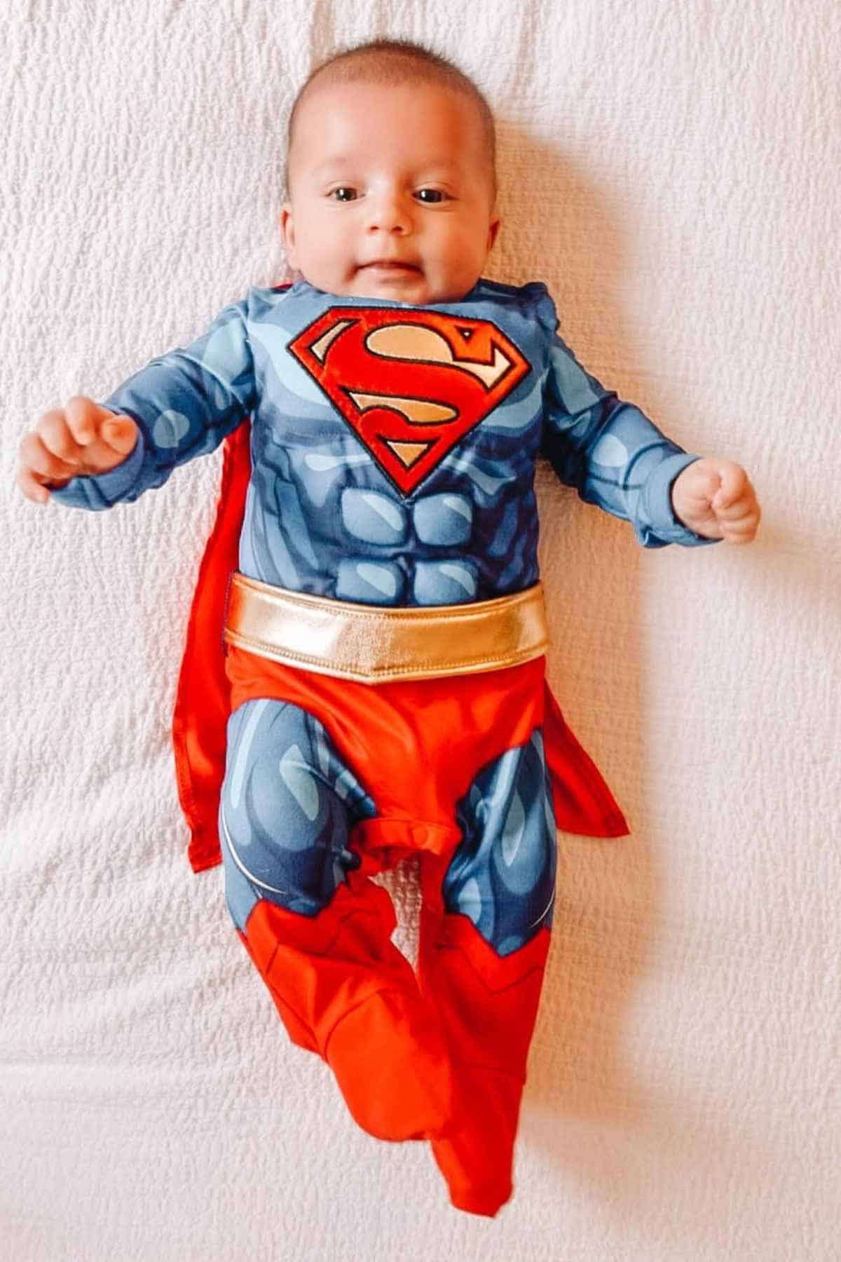 A baby on bed dressed in a superman suit.