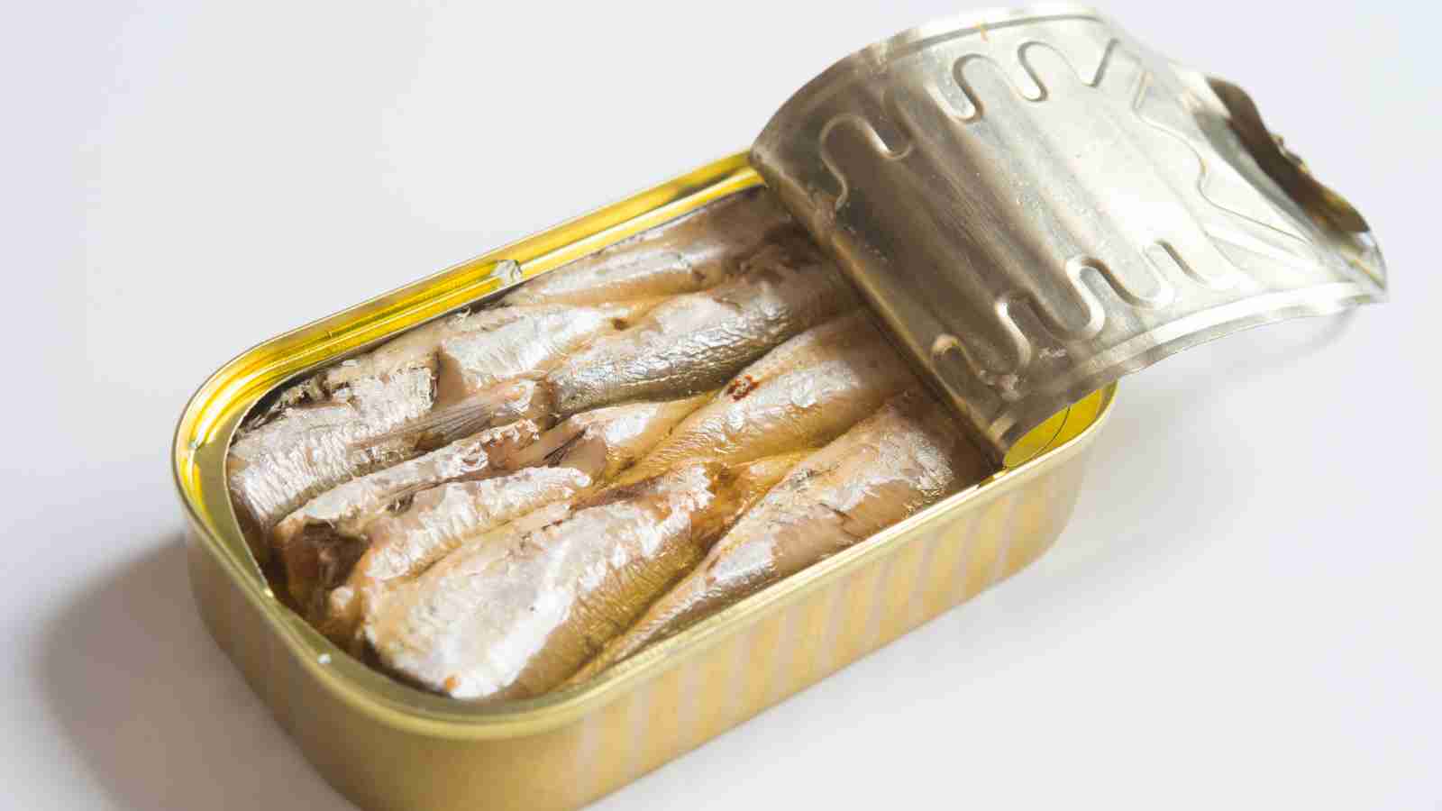 A partially opened tin of sardines is shown on a white background.