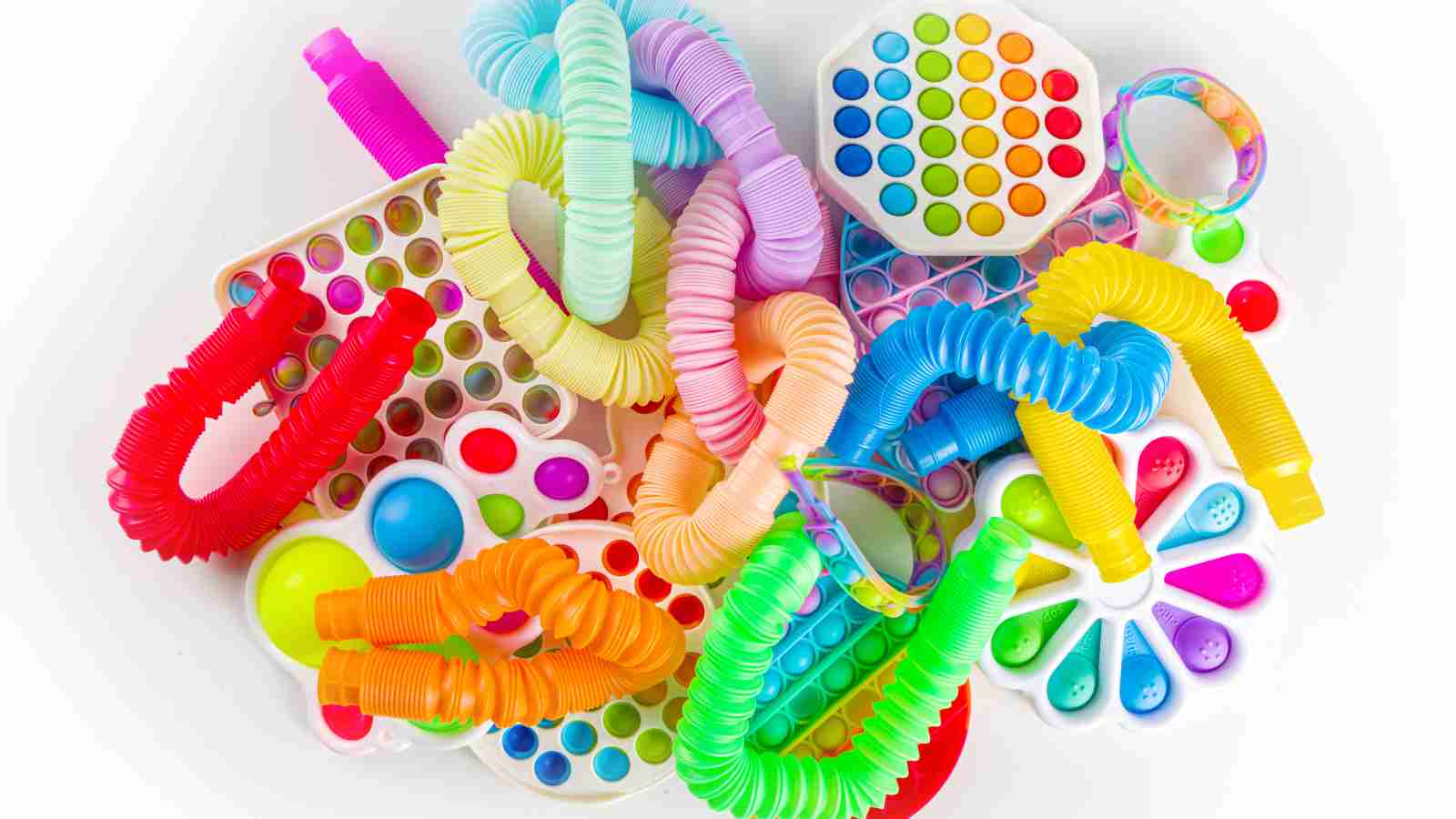 A collection of colorful sensory fidget toys, including pop-its, tubes, and spinners, arranged on a white background.