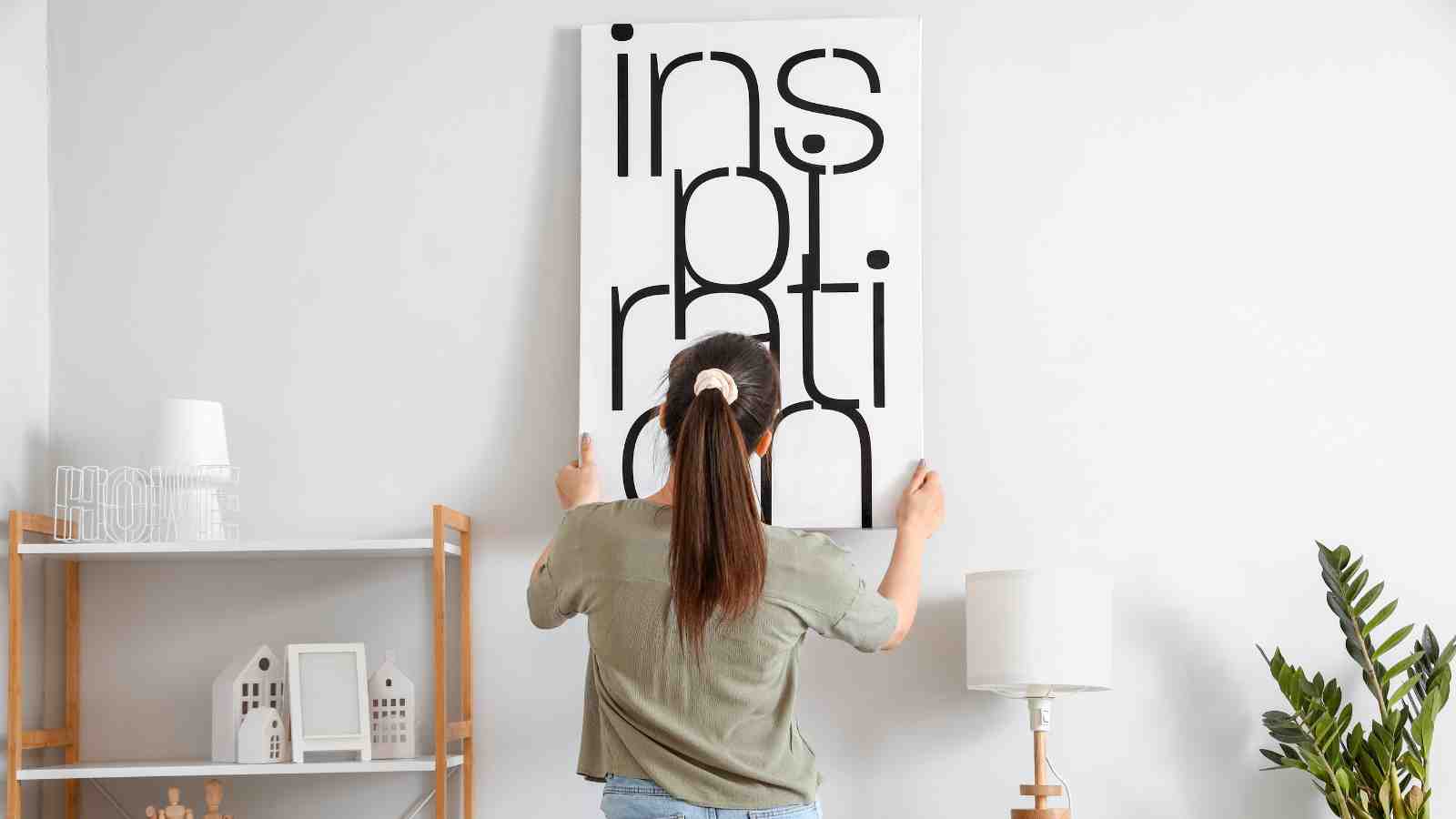 A woman hangs a framed print with the word "Inspiration" on a wall.