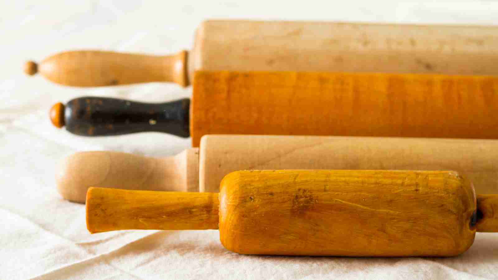 Four wooden rolling pins of varying sizes and colors are arranged on a white surface.
