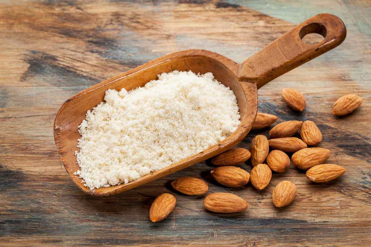 Almond flour in a wooden container with some whole almonds around it, place in a wooden surface.