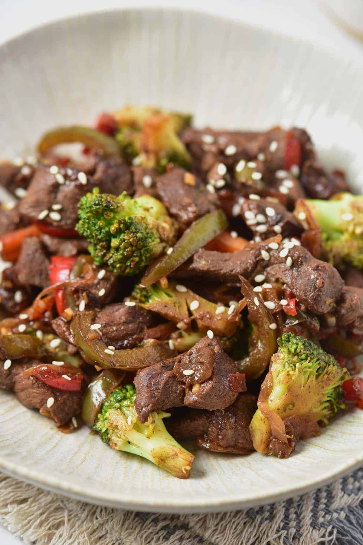 Center shot angle of venison stir fry served on a white textured plate, with a table mat underneath.