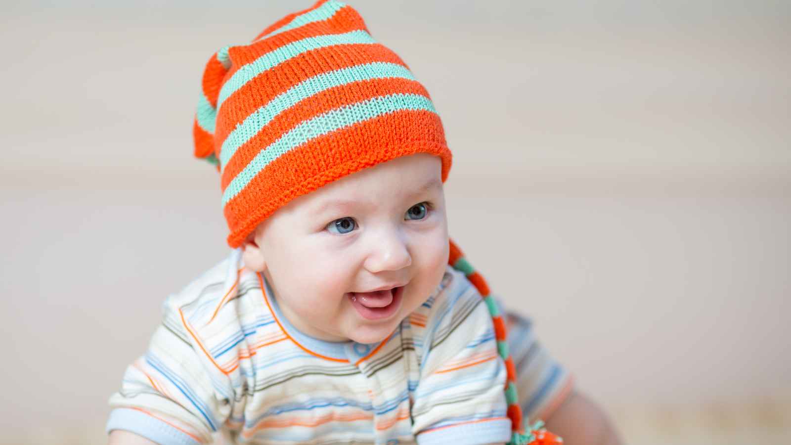 A baby crawling wearing a colorful clothe and bonnet.