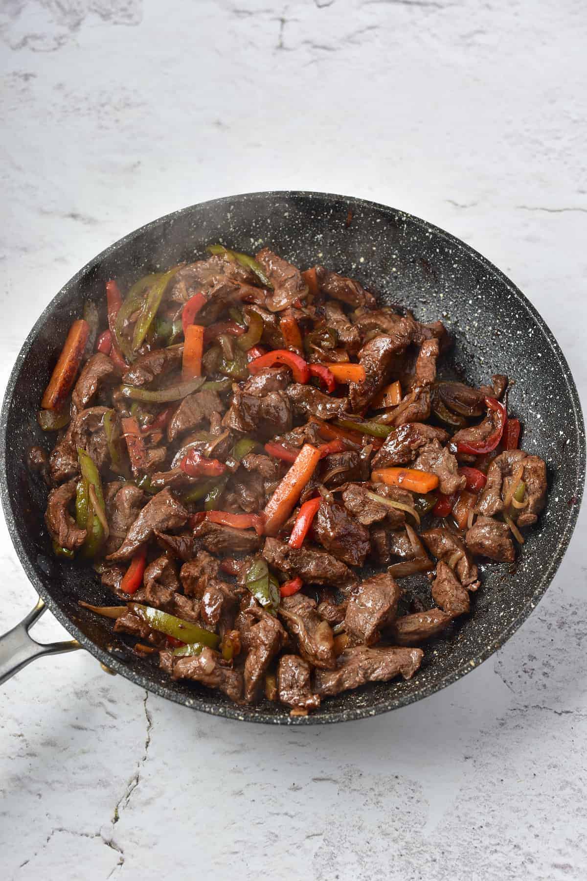 Freshly cooked venison stir fry in a pan, set on a marble surface.