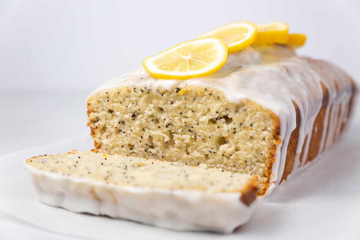 A loaf of lemon poppy seed bread with a slice cut out.
