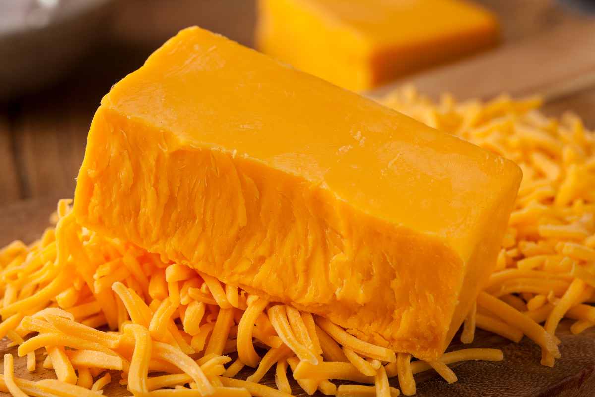 A sharp cheddar cheese, half solid and the other are shredded.