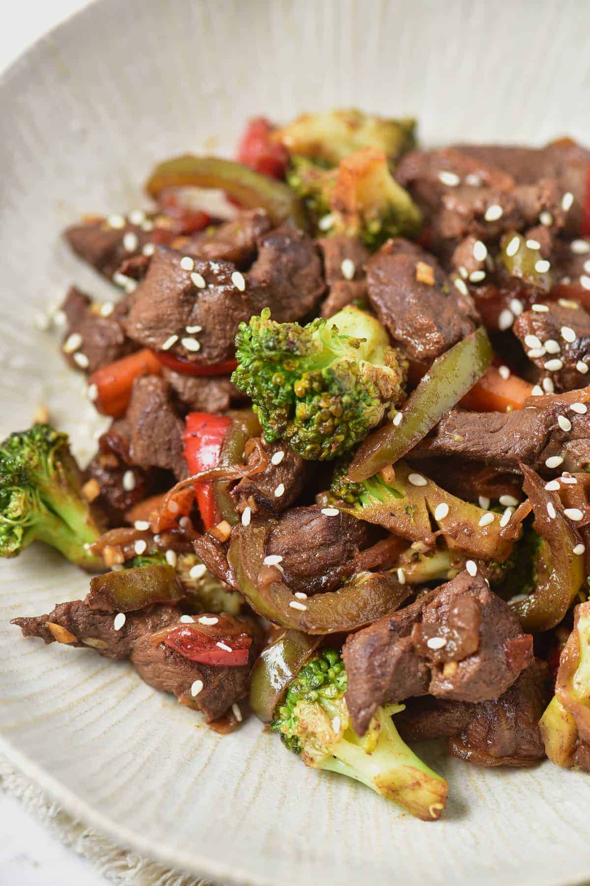 Close-up shot of venison stir fry plated with broccoli and a sprinkle of sesame seeds on a white textured dish.